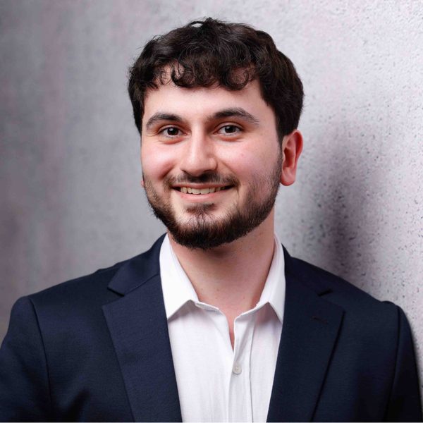 Porträt von Hüseyin Robin Tokgöz im dunklen Sakko vor heller Betonwand